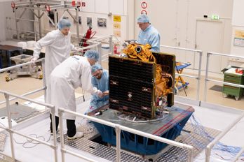 Preparing_Arctic_Weather_Satellite_for_tests.jpg Fyra personer står och arbetar på en satellit i ett renrum.