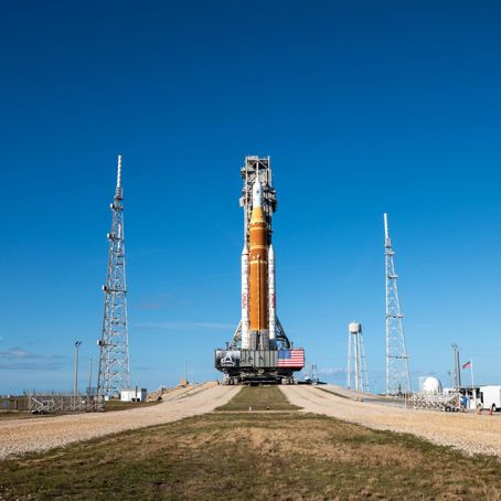 KSC-01172026-Artemis II_Rollout-24~large.jpg En raket på marken mot en blå himmel