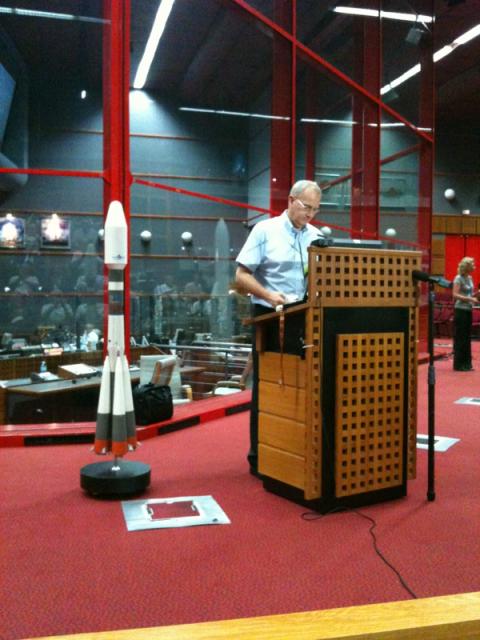 Arianespace vd Jean-Yves LeGall, bredvid en modell av en Soyuz-raket, meddelar att uppsändningen är framflyttad 24 tim.