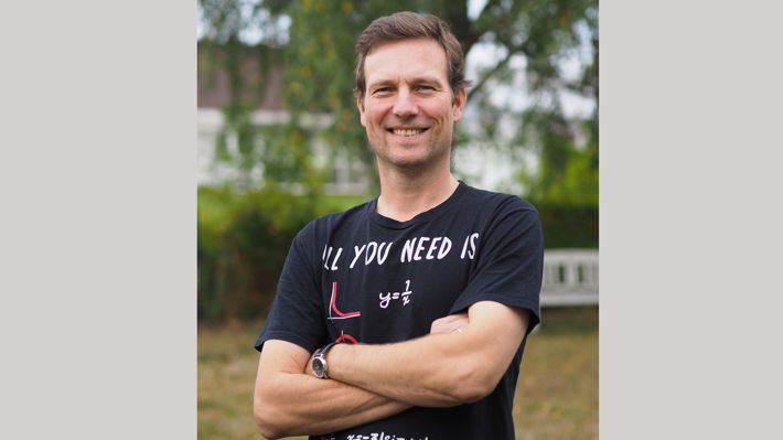 En man står med korsade armar med blå tshirt. Han ler och ser glad ut.