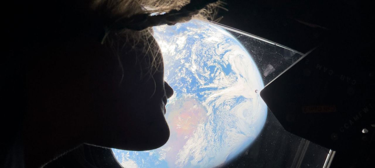 Christina Koch i Orion.jpg En kvinna som tittar ut genom ett fönster mot jorden