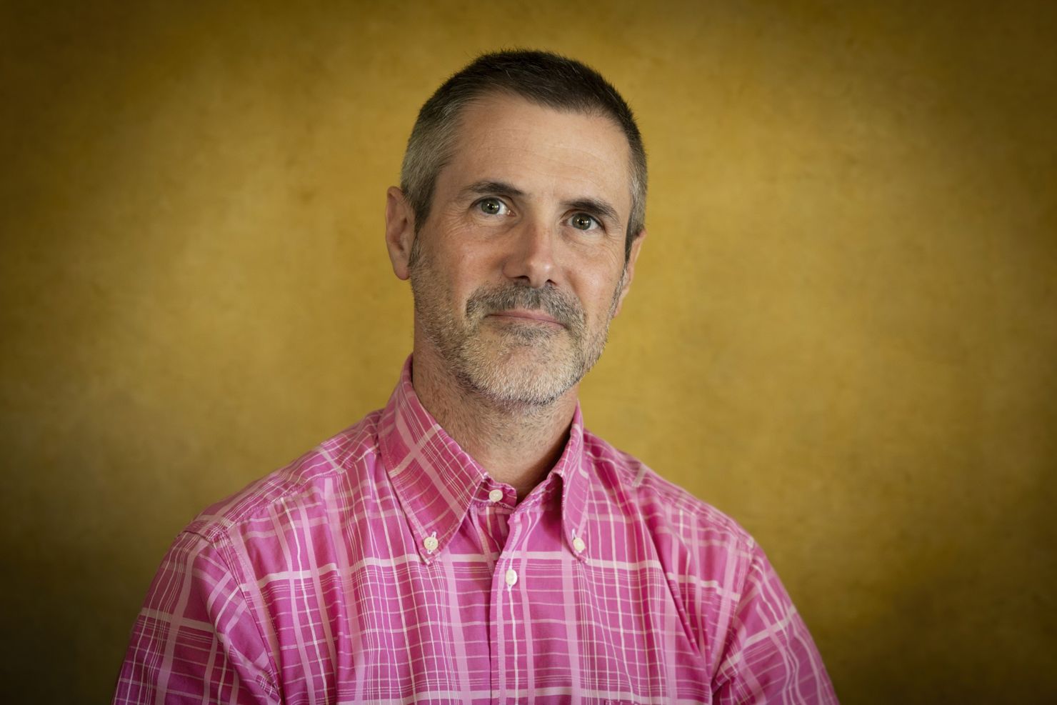 Renaud Merle.jpg En man som tittar in i kameran med en rosa skjorta på sig mot gul bakgrund.