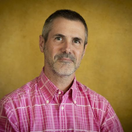 Renaud Merle.jpg En man som tittar in i kameran med en rosa skjorta på sig mot gul bakgrund.