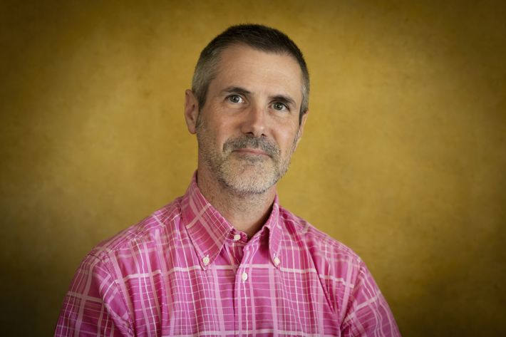 Renaud Merle.jpg En man som tittar in i kameran med en rosa skjorta på sig mot gul bakgrund.