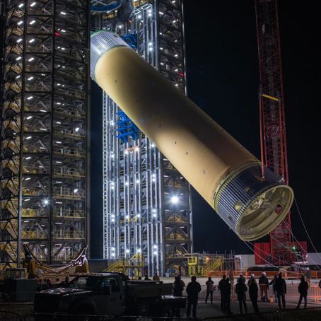 SLS core stage.jpg Ett stort rör som monteras på en enorm ställning av byggarbetare.