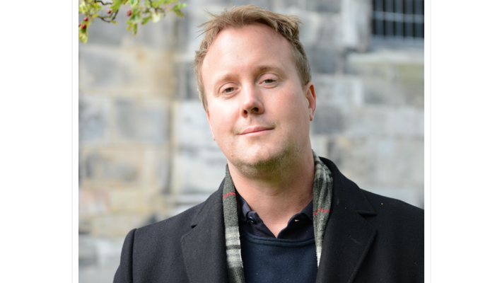 Porträtt på Oscar Agertz. Vit man men blå kavaj och halsduk.