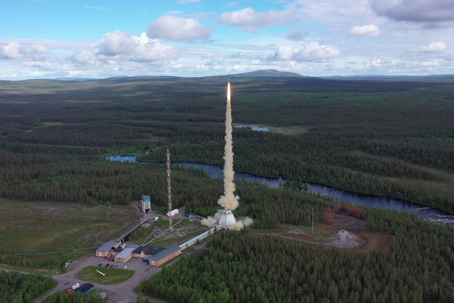 MASER14_vlcsnap-2019-07-04-09h33m24s373.png En raket lyfter från en rymdbas omgiven av granskog och älvar.
