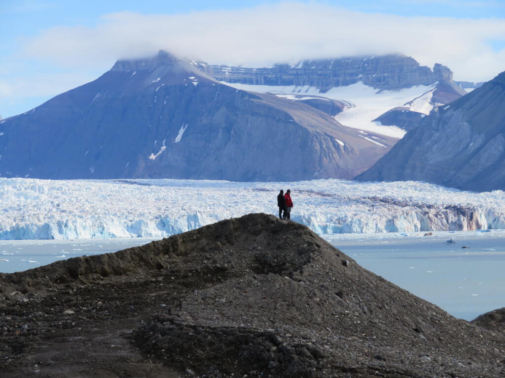 Två personer som står på en kulle bredvid en glaciär.