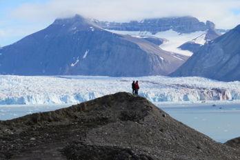 Cyntia på Svalbard.jpg Två personer som står på en kulle bredvid en glaciär.