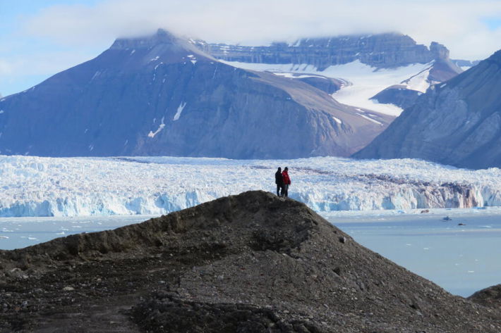 Cyntia på Svalbard.jpg Två personer som står på en kulle bredvid en glaciär.
