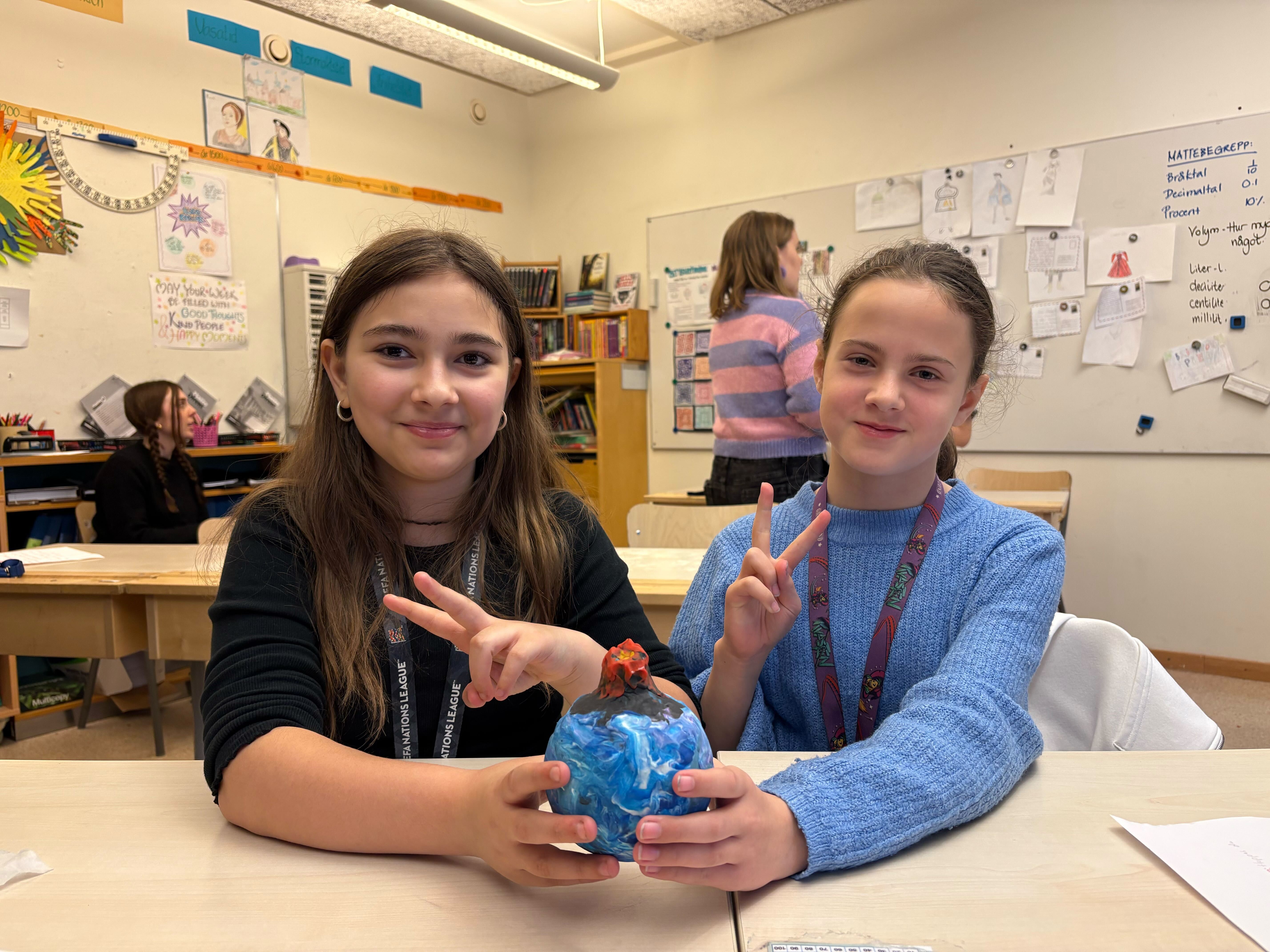 Två flickor gör två fingrar upp med en pysslad planet i handen