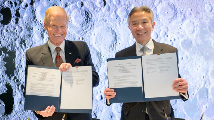 NASA:s administratör Bill Nelson till vänster och Japans minister för utbildning, kultur, sport, vetenskap och teknik, Masahito Moriyama till höger. De båda ler och håller upp en kopia ett avtalet.