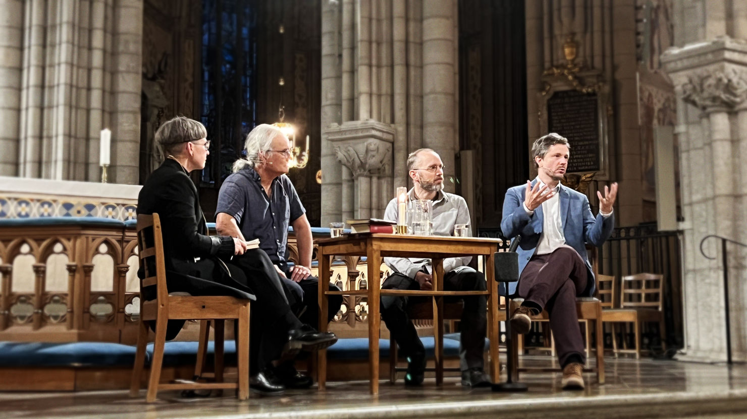 Paneldeltagarna sitter på stolar runt ett bord framför altaret i uppsala domkyrka. Från vänster samtalsledaren och prästen Kerstin Dillmar, fil dr i religionsfilosofi Oliver Li, lektor i filosofi Sebastian Lutz och docent i astronomi Martin Sahlén.