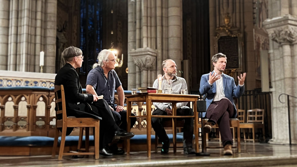 Paneldeltagarna sitter på stolar runt ett bord framför altaret i uppsala domkyrka. Från vänster samtalsledaren och prästen Kerstin Dillmar, fil dr i religionsfilosofi Oliver Li, lektor i filosofi Sebastian Lutz och docent i astronomi Martin Sahlén.