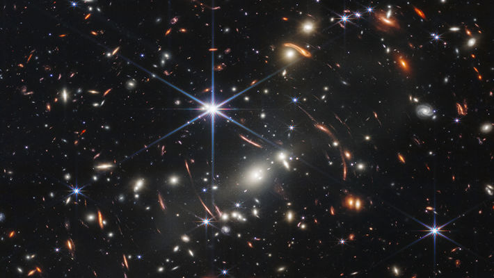 Bilden visar SMACS 0723, ett kluster av galaxer mot en svart bakgrund.