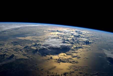 En bild av jorden tagen från den internationella rymdstationen. På bilden syns jordens runda form mot rymdens svarta bakgrund. På planeten syns vatten och moln. Solens ljus reflekteras i vattnet.