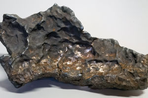 Meteoriten i Enköping Den ojämna, mörkgråa meteoriten med metalliskt skimmer och gropar i ytan, liggande på ett ljust underlag.