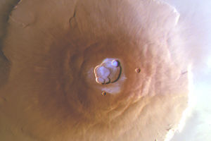 Olympus Mons, Mars Express En bild av vulkanen Olympus Mons på Mars tagen ovanifrån. Den brunröda vulkanen breder ut sig över ytan, och i höjden på mitten av vulkanen finns en urholkning som liknar en krater. I denna krater syns vattenis som ett tunt, ljusblått lager som kontrasterar mot den annars enfärgade vulkanen.